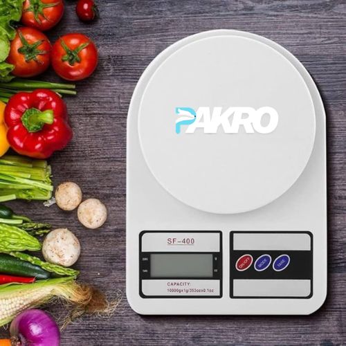 Digital kitchen scale with 'PAKRO' branding surrounded by fresh vegetables on a wooden surface