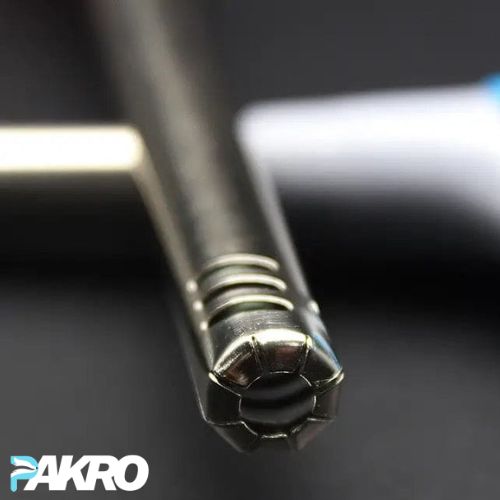 Close-up of a metal rod with a textured end, branded 'PAKRO', on a dark background.