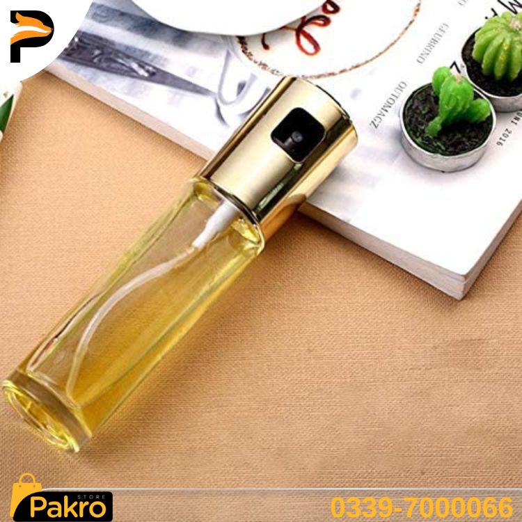 Gold and clear spray bottle on a textured surface with a magazine and small potted plant in the background.