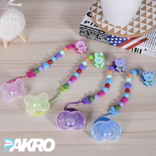 Colorful baby pacifier holder with teddy bear clips on a wooden surface, featuring the brand 'PAKRO'.