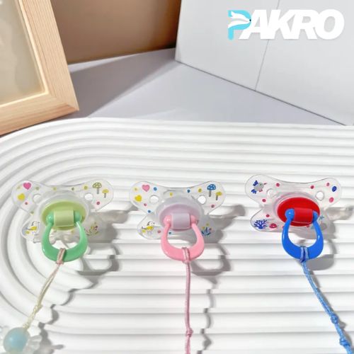 Premium Baby Pacifier with Teether and Clip - Comfortable for 0-3 Months - Three colorful pacifiers with holders on a textured surface, branded 'PAKRO'.